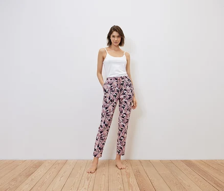 Une femme se tient debout, les mains dans les poches d'un pantalon à fleurs, haut blanc.