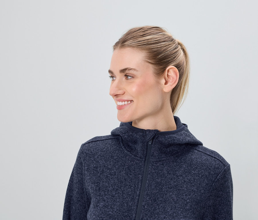 Profil d'une femme souriante aux cheveux blonds portant un sweat à capuche zippé bleu.