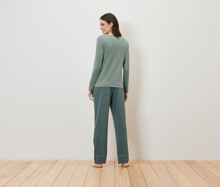 Une femme en pyjama vert à manches longues et pantalon à motifs, vue de dos.
