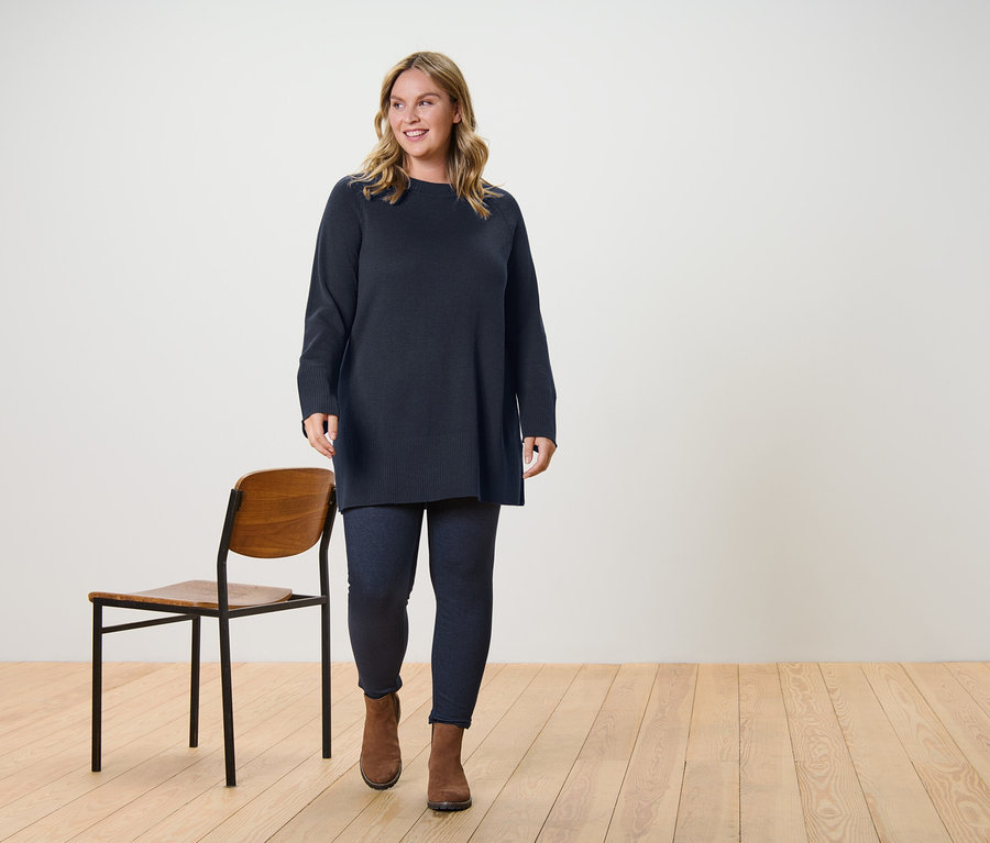 Une femme marche et porte un long pull en maille marron foncé et un legging doublé à l’aspect jean.