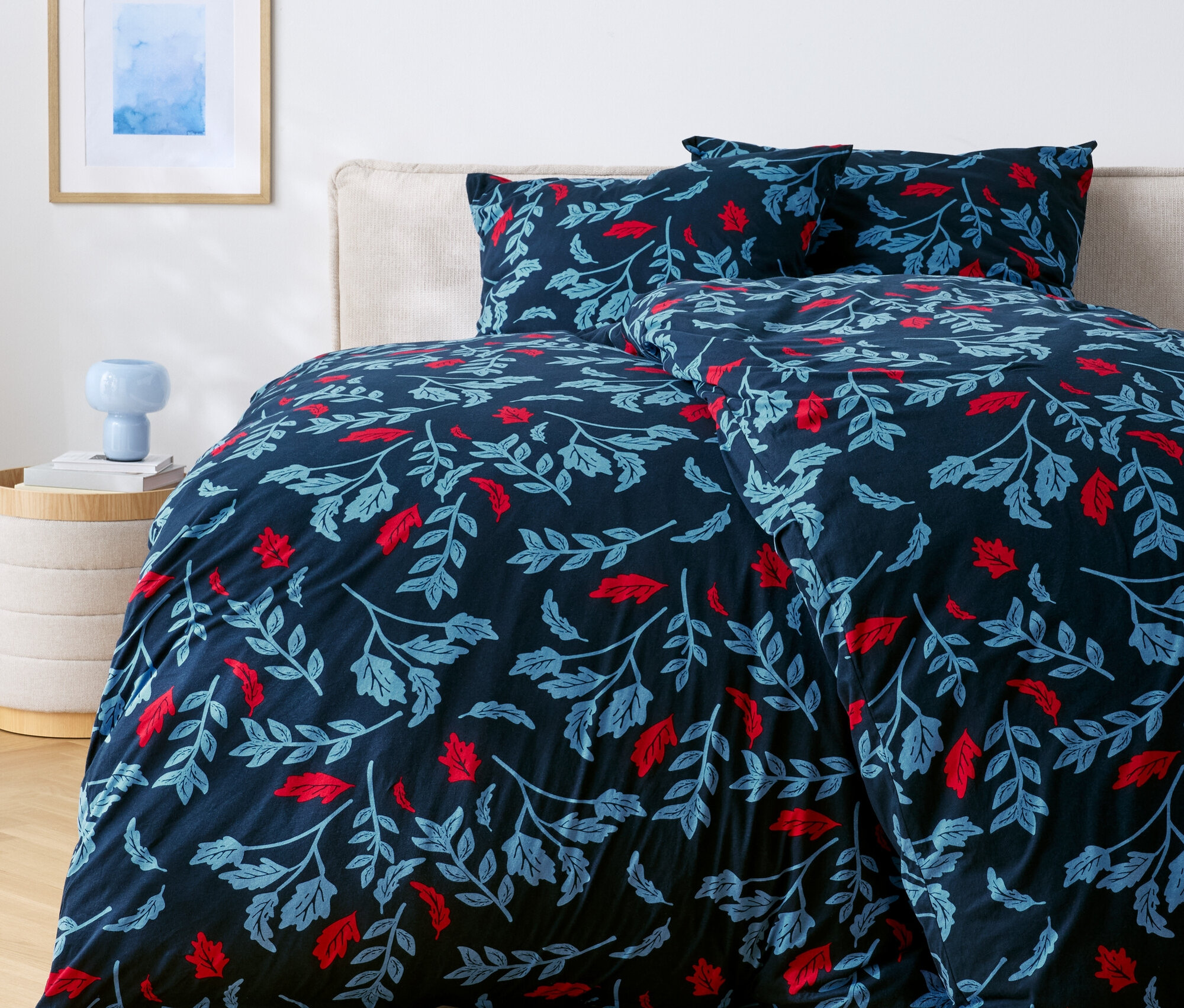 Lit avec des draps bleu foncé avec des feuilles rouges et bleues.