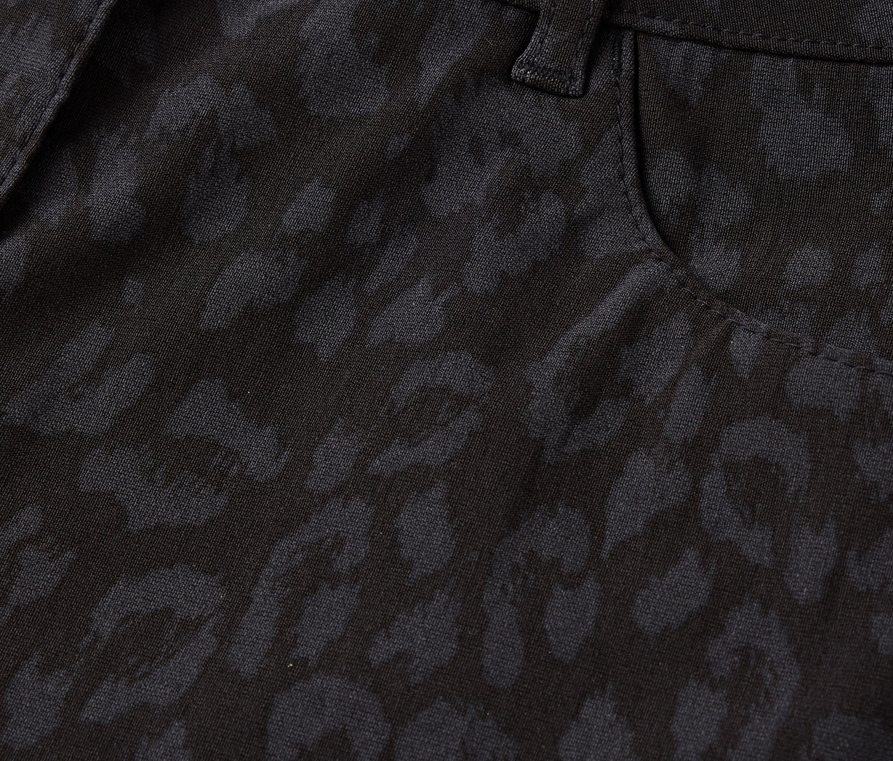 Gros plan sur un pantalon noir à motif léopard, avec un bouton et une poche.