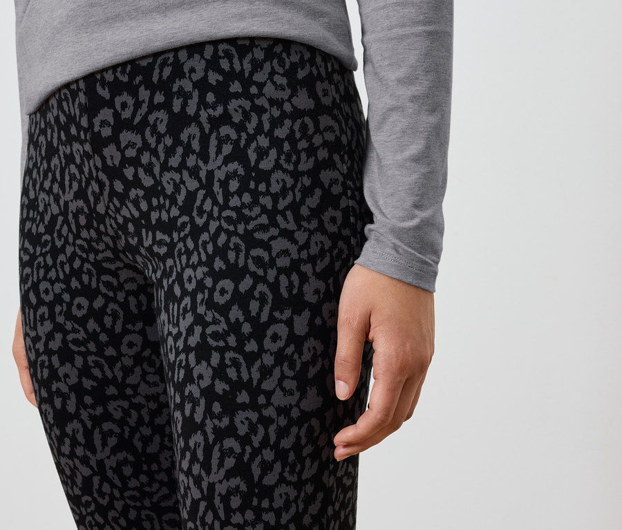 Gros plan d'une personne portant un legging noir avec un imprimé animal gris et un t-shirt gris à manches longues.