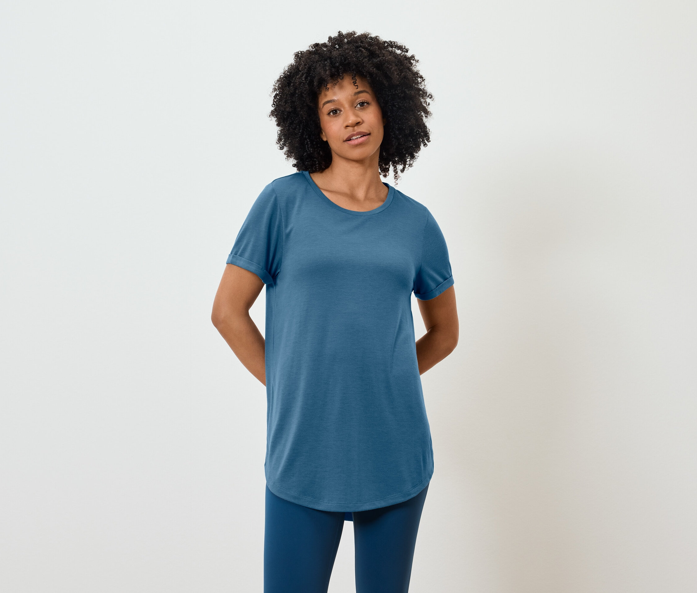 Une afro-américaine portant un t-shirt bleu et des leggings pose sur un fond blanc.