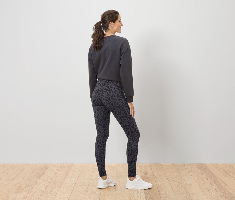 Femme posant en pull gris et leggings léopard.