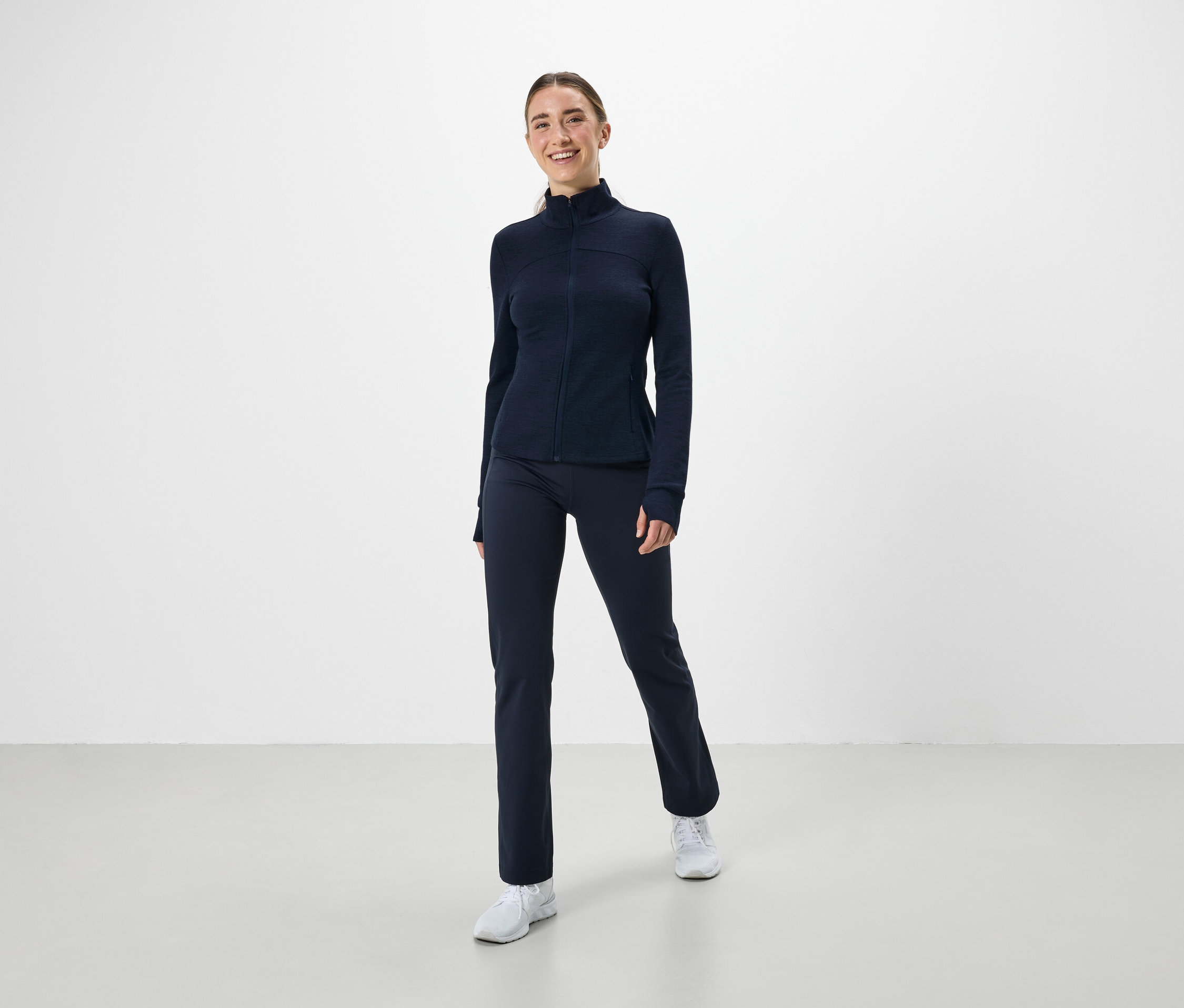 Une femme porte un ensemble de sport bleu marine et des baskets blanches.