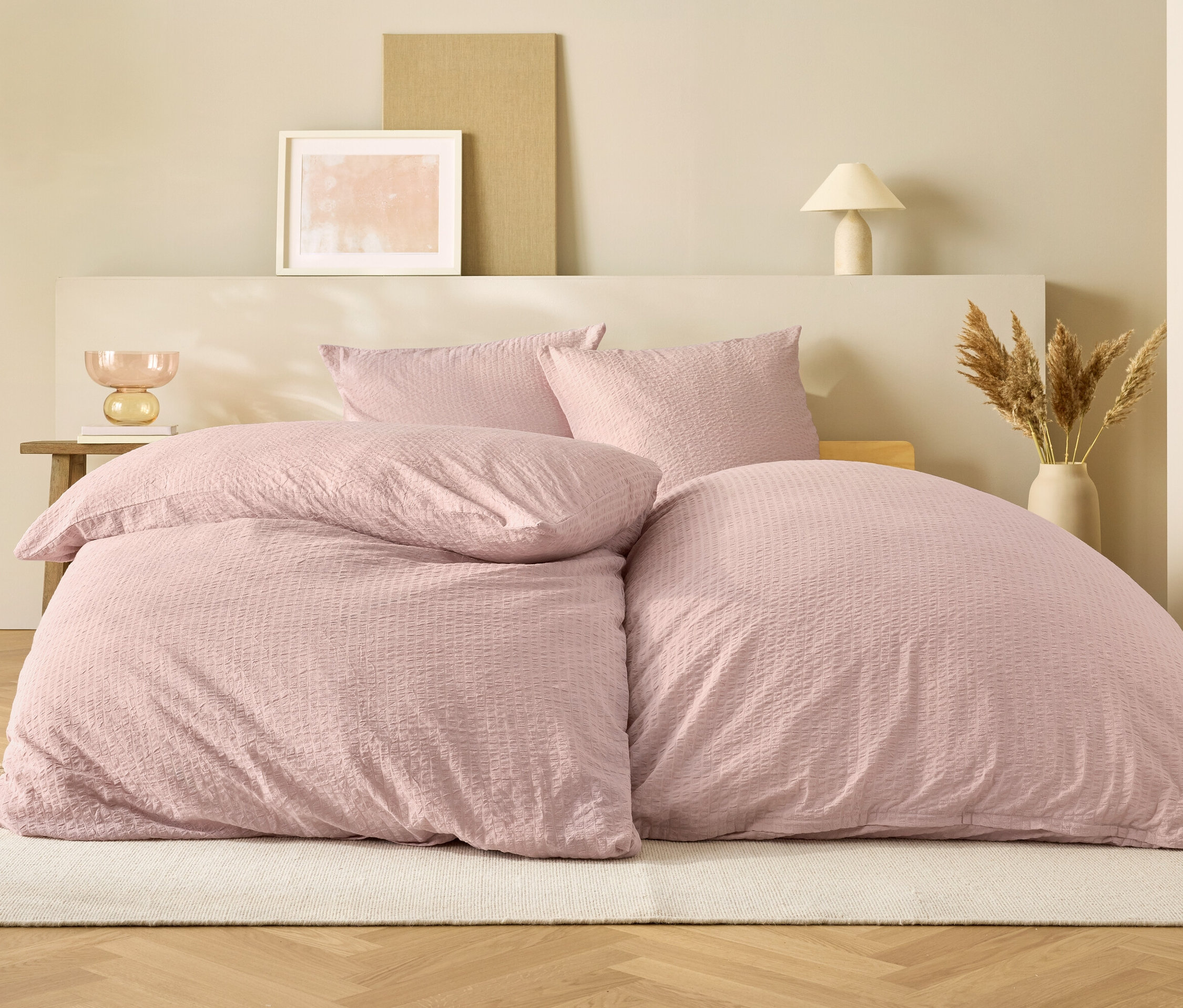 Linge de lit rose sur un lit devant un fond beige.