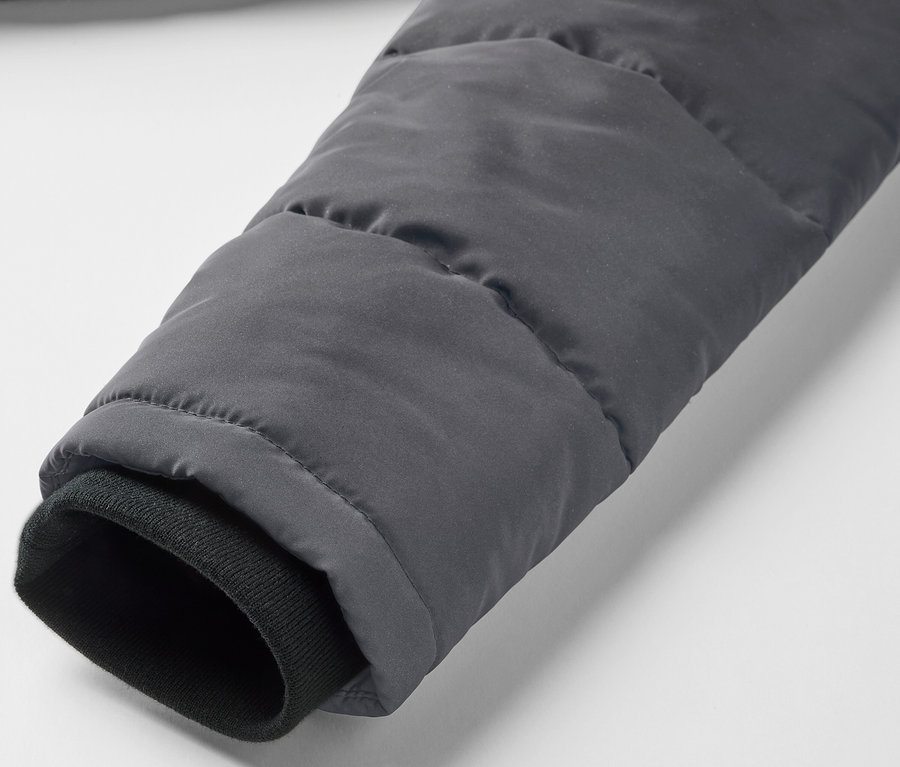 Gros plan sur la manche d'une veste matelassée grise pour enfant avec des éléments réfléchissants et un poignet noir.