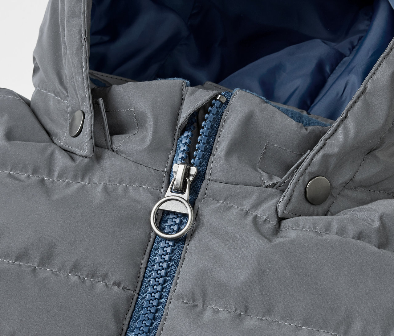Gros plan sur une Veste matelassée réfléchissante pour enfant grise avec une fermeture éclair bleue.