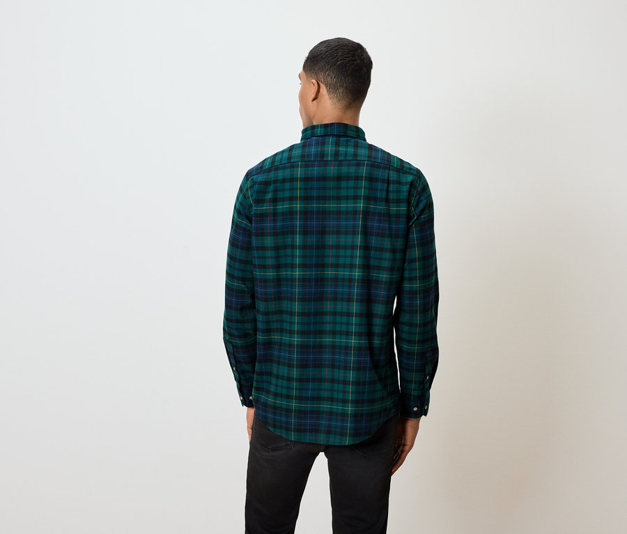 Un homme, vu de dos, porte une chemise à carreaux verte et un jean noir.