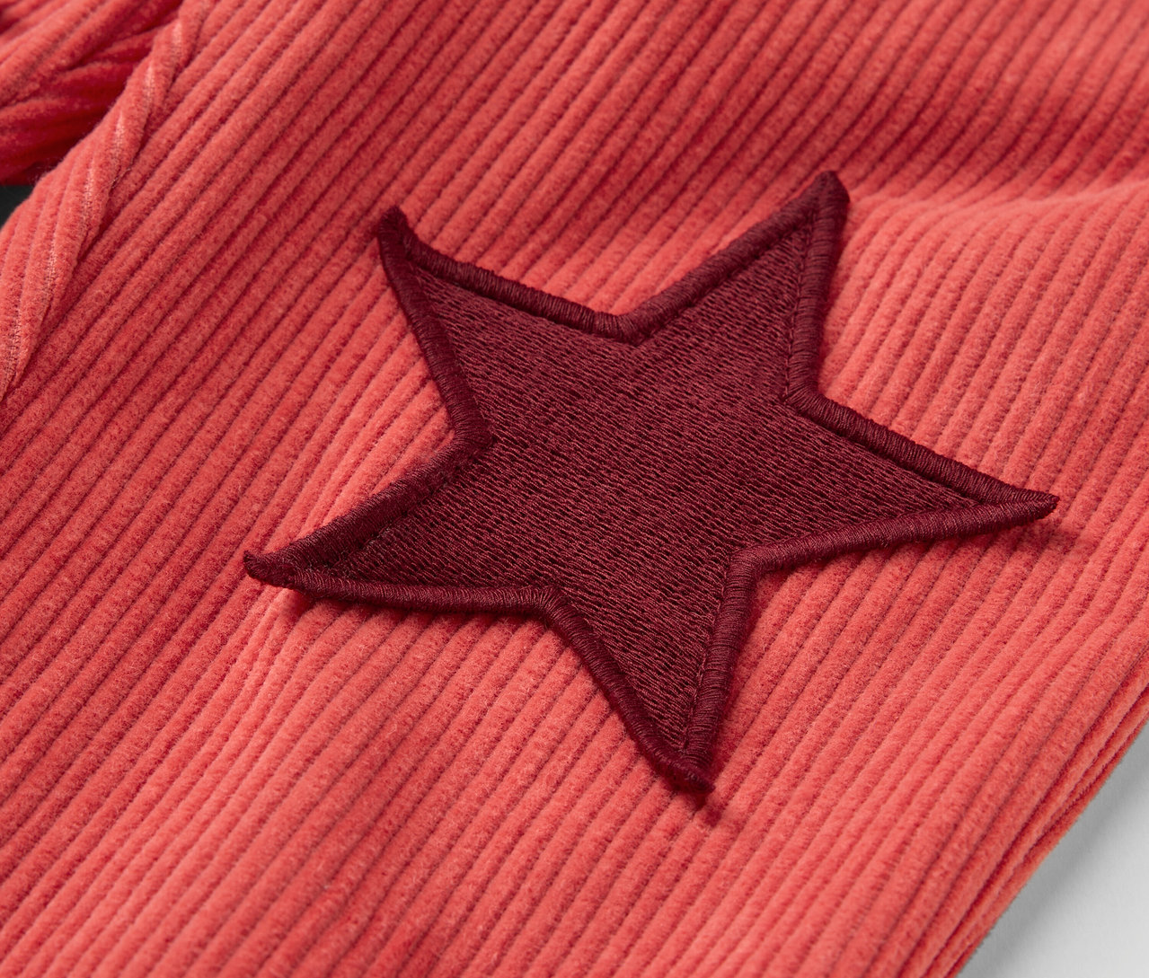 Détail d'un pantalon en velours rouge pour enfant avec une étoile rouge foncé.