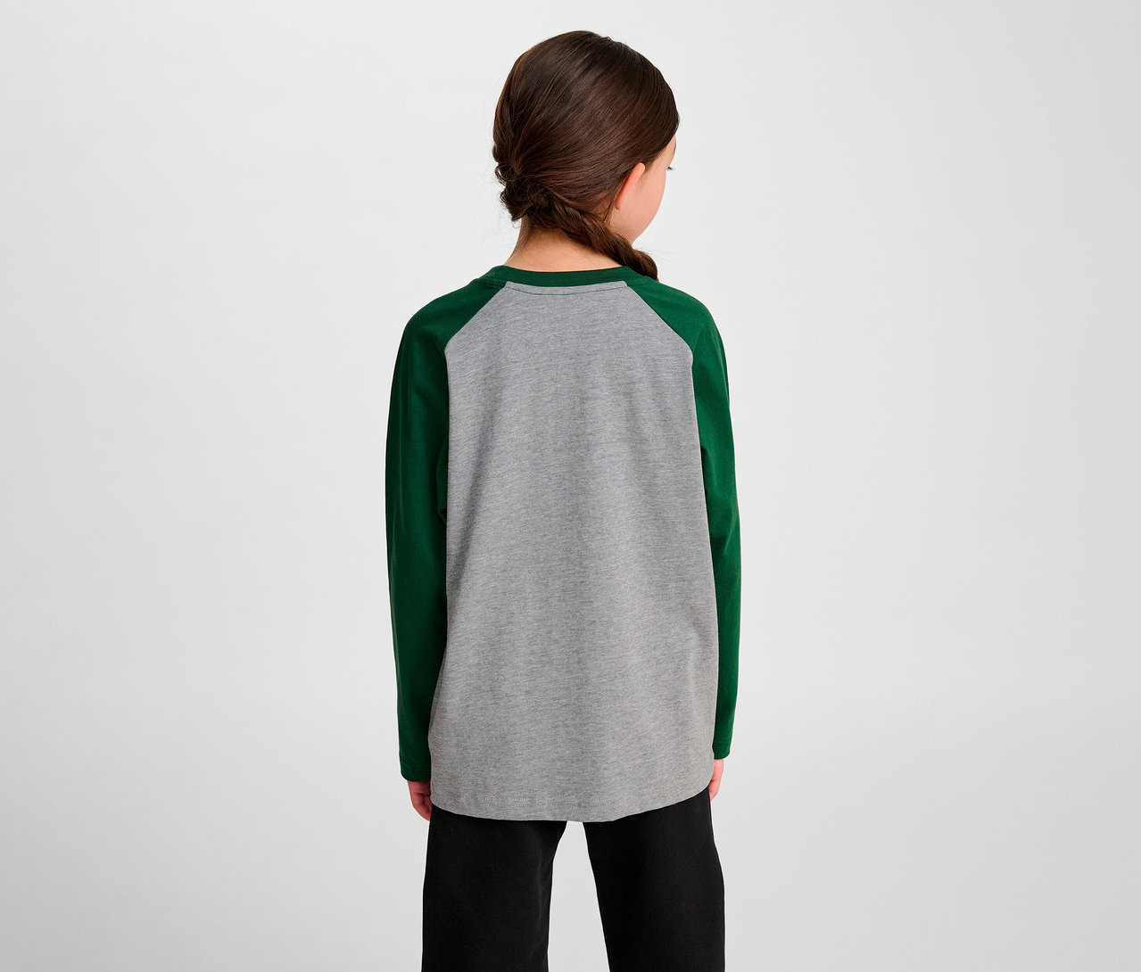 Une fille vue de dos porte un t-shirt ample à manches raglan HUMMEL HMLJR BEE vert et un pantalon noir.