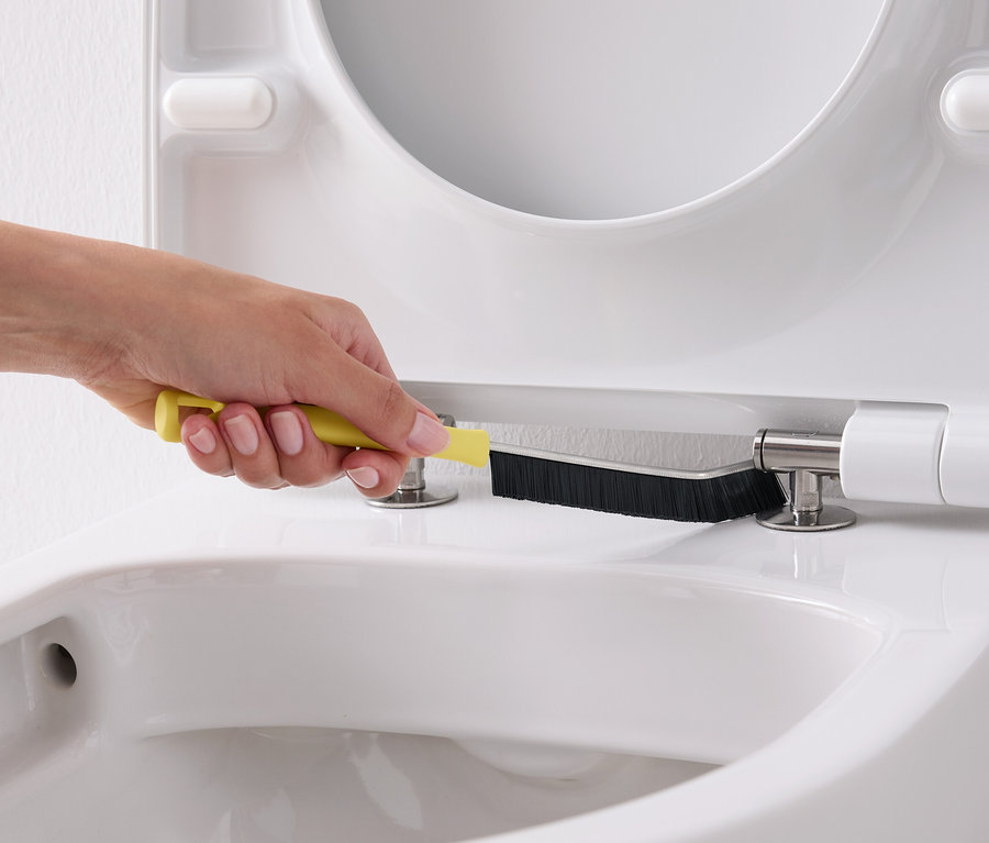 Une main nettoie un siège de toilette blanc avec une brosse jaune.