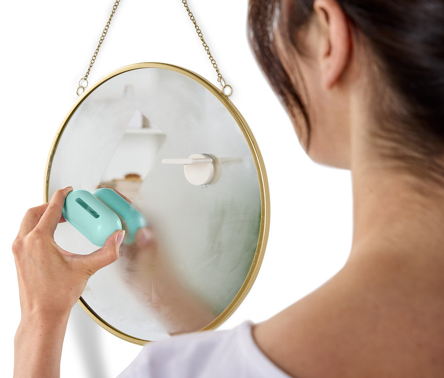 Une femme nettoie un miroir rond accroché au mur avec un nettoyant bleu.