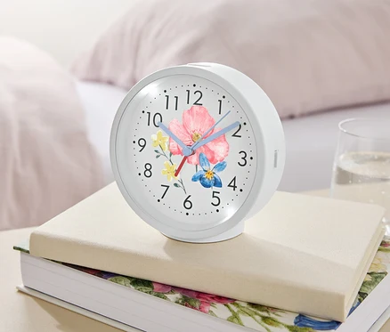 Un réveil blanc avec un motif floral repose sur des livres à côté d'un verre d'eau.