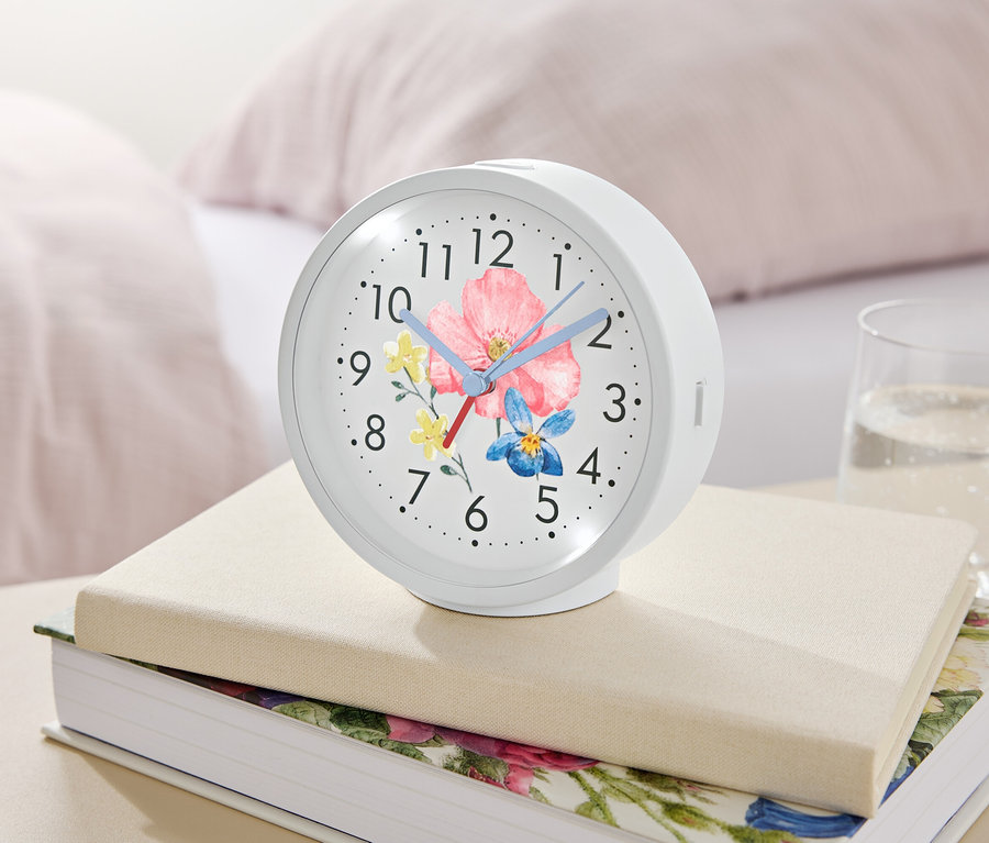 Un réveil blanc avec un motif floral repose sur des livres à côté d'un verre d'eau.