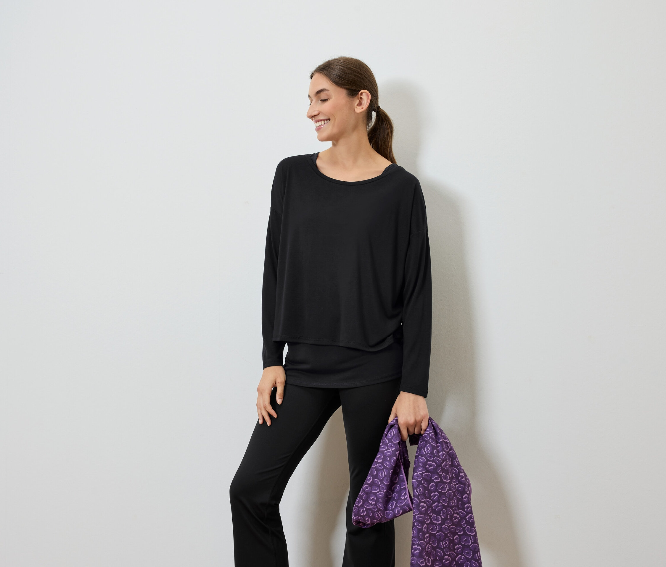 Femme souriante vêtue de noir tenant un sac violet.