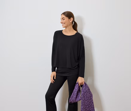 Femme souriante vêtue de noir tenant un sac violet.
