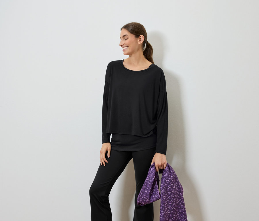 Femme souriante vêtue de noir tenant un sac violet.