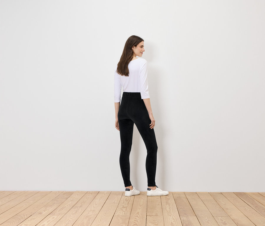 Une femme portant des leggings noirs et un haut blanc se tient dos à la caméra.