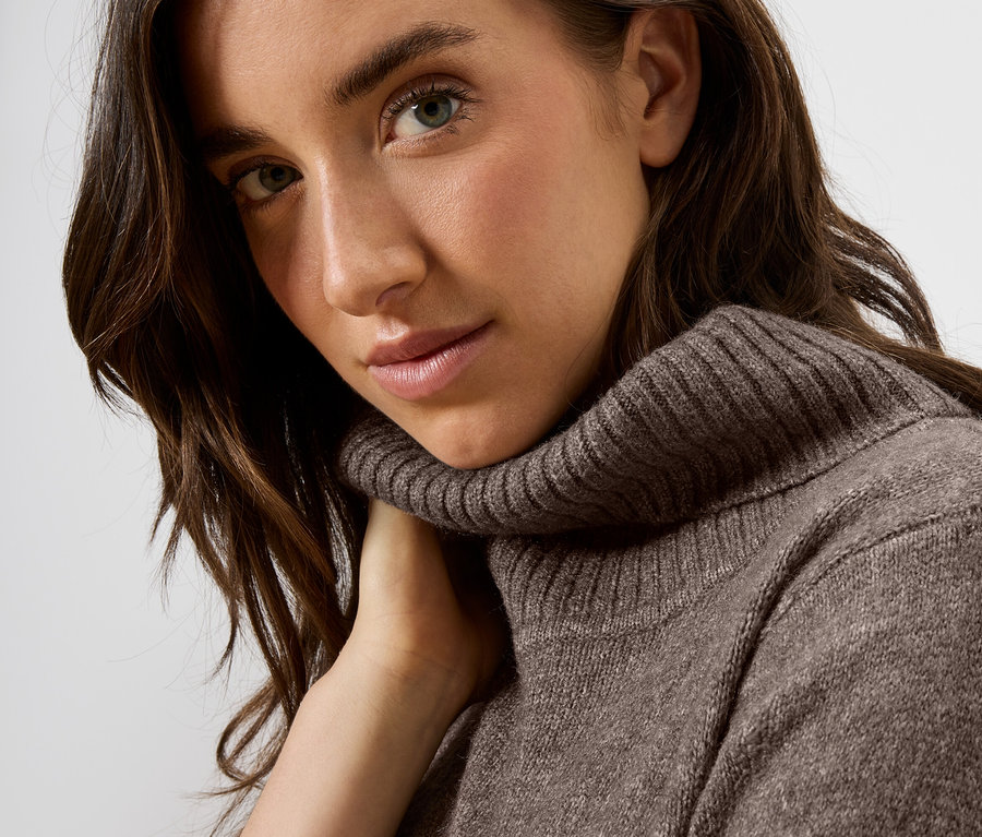 Portrait d'une femme aux cheveux bruns portant un pull à col roulé marron.