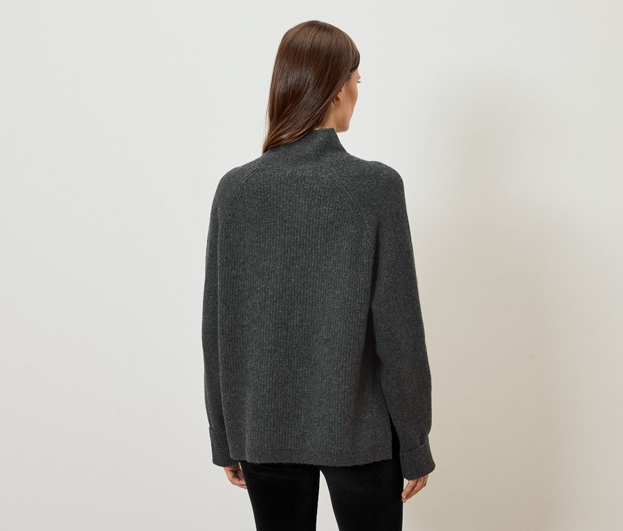 Une femme, de dos, porte un pull gris.