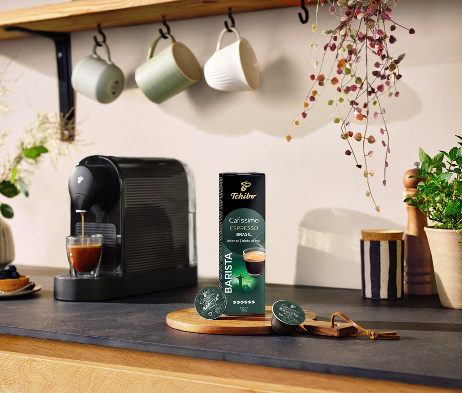 Une machine à café noire prépare du café dans un verre à côté d'un paquet de 10 capsules Espresso Brasil.