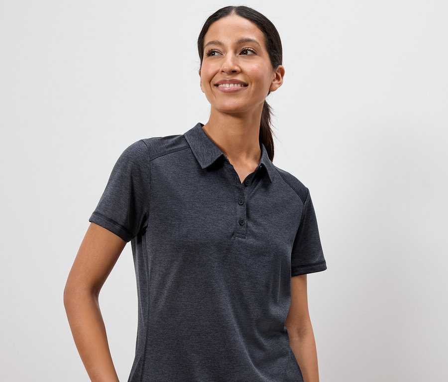 Une femme porte un polo gris foncé sur un fond blanc.