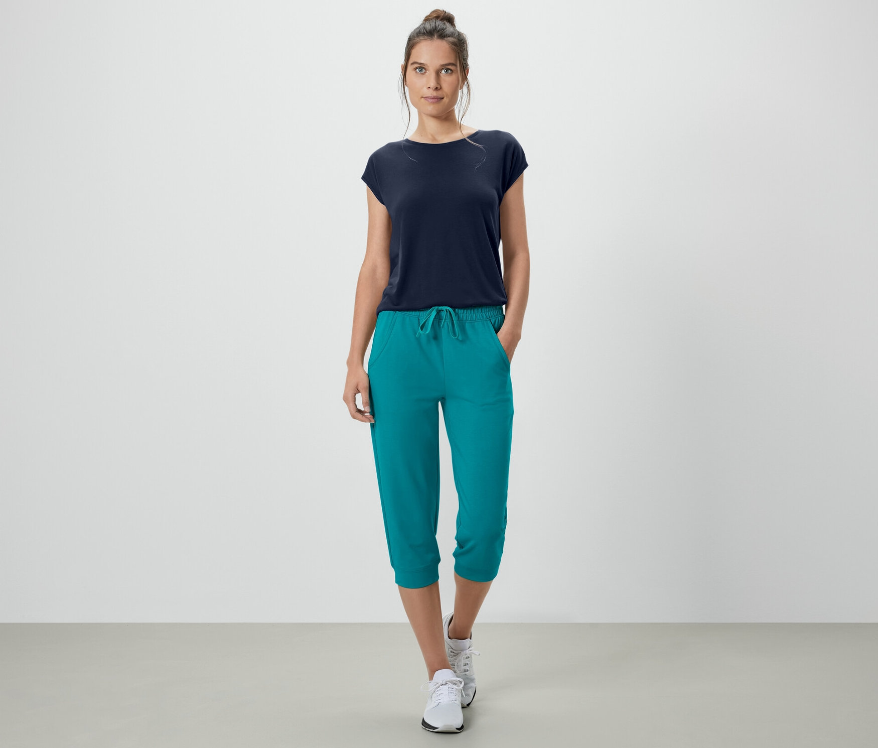Femme debout avec les mains dans les poches d'un pantalon sweat 3/4 turquoise.
