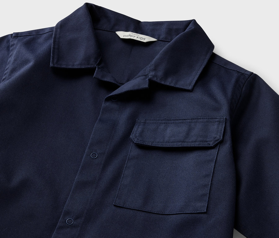 Gros plan sur une chemise pour enfant bleue à manches courtes avec une poche.