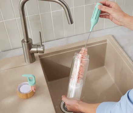 Une femme nettoie une bouteille avec la brosse à vaisselle pour verres et bouteilles 3 en 1.