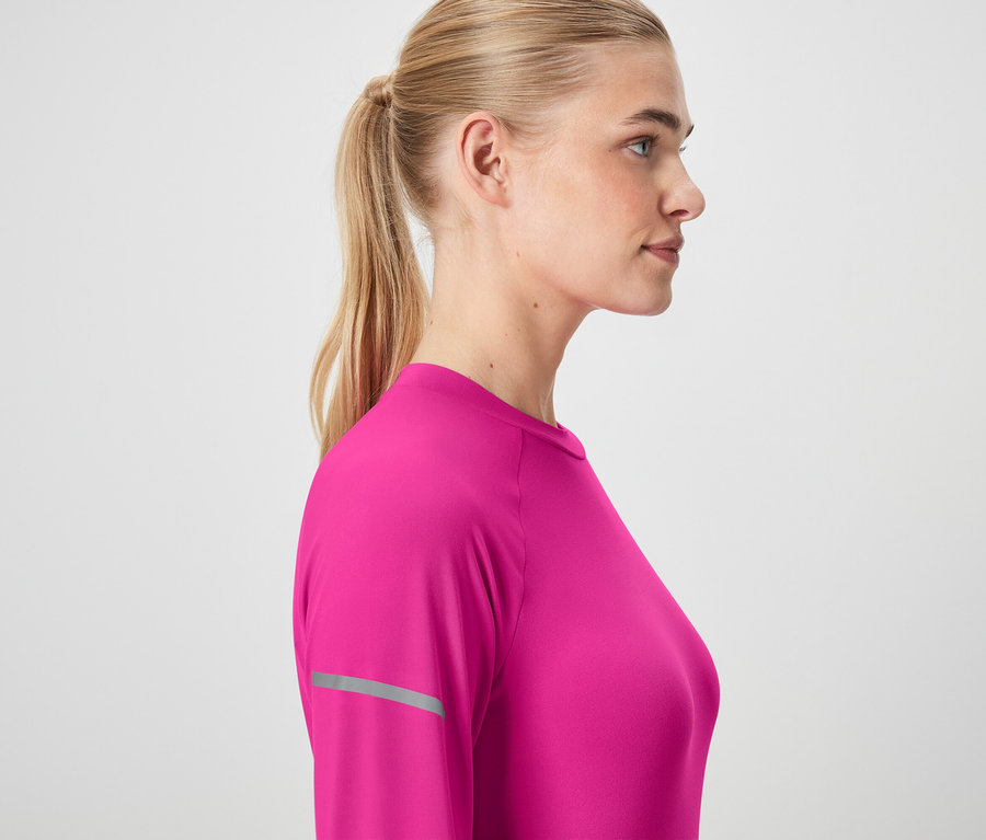 Profil d'une femme blonde aux cheveux attachés en queue de cheval, portant un t-shirt rose à manches longues.
