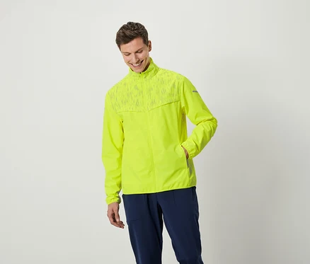 Un homme souriant pose en veste jaune néon et pantalon bleu marine.