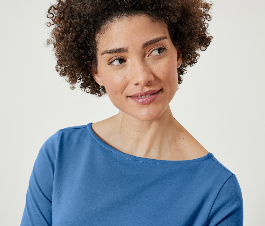 Une femme aux cheveux bruns et bouclés porte un t-shirt bleu à manches trois-quarts.