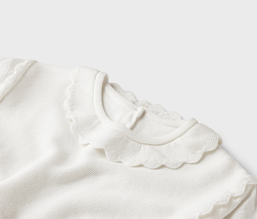 Gros plan d'un pull en tricot blanc avec un col ondulé.
