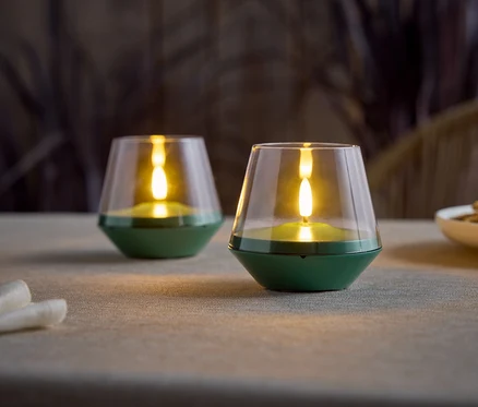 Deux bougies LED vertes à piles avec un dessus en verre transparent sont posées sur une table.