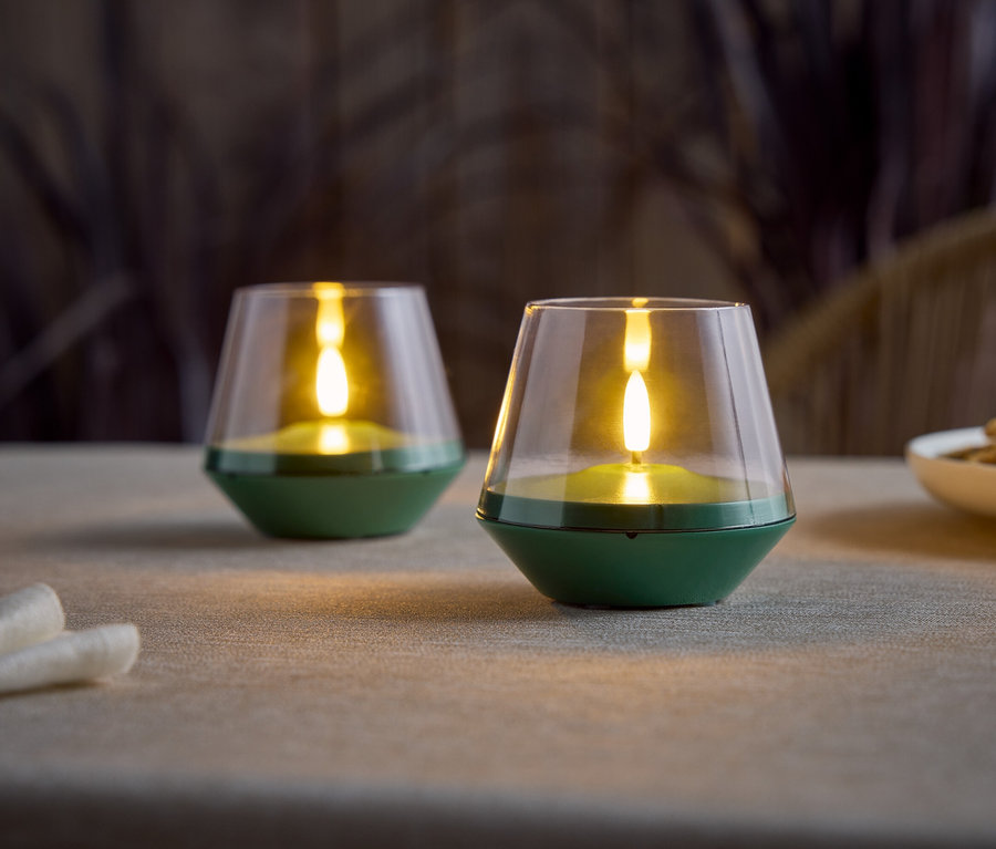 Deux bougies LED vertes à piles avec un dessus en verre transparent sont posées sur une table.