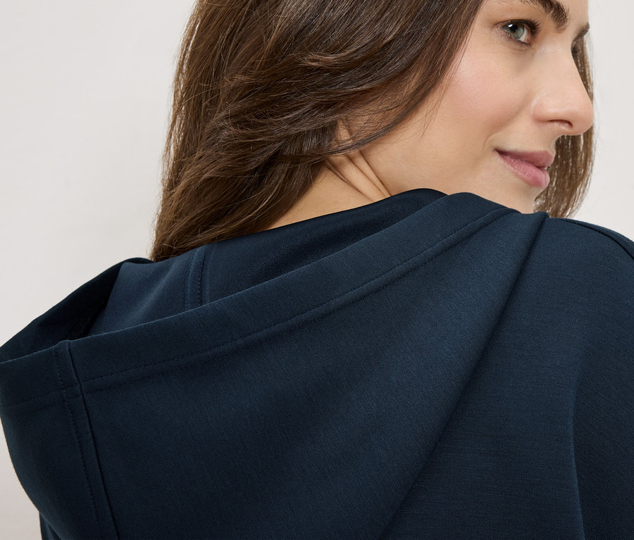 Femme portant un sweat à capuche bleu marine, regardant par-dessus son épaule.