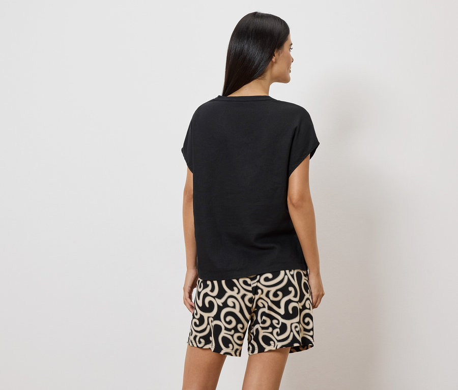 Femme vue de dos portant un t-shirt noir et un short à motifs sur fond blanc.