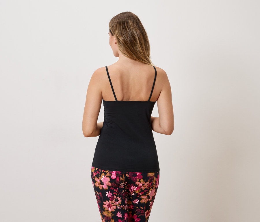 Vue de dos d'une femme aux longs cheveux blonds portant un débardeur noir et un pantalon à fleurs.