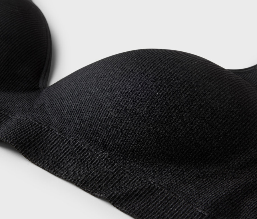Gros plan d'un soutien-gorge noir côtelé avec des bretelles sur un fond neutre.