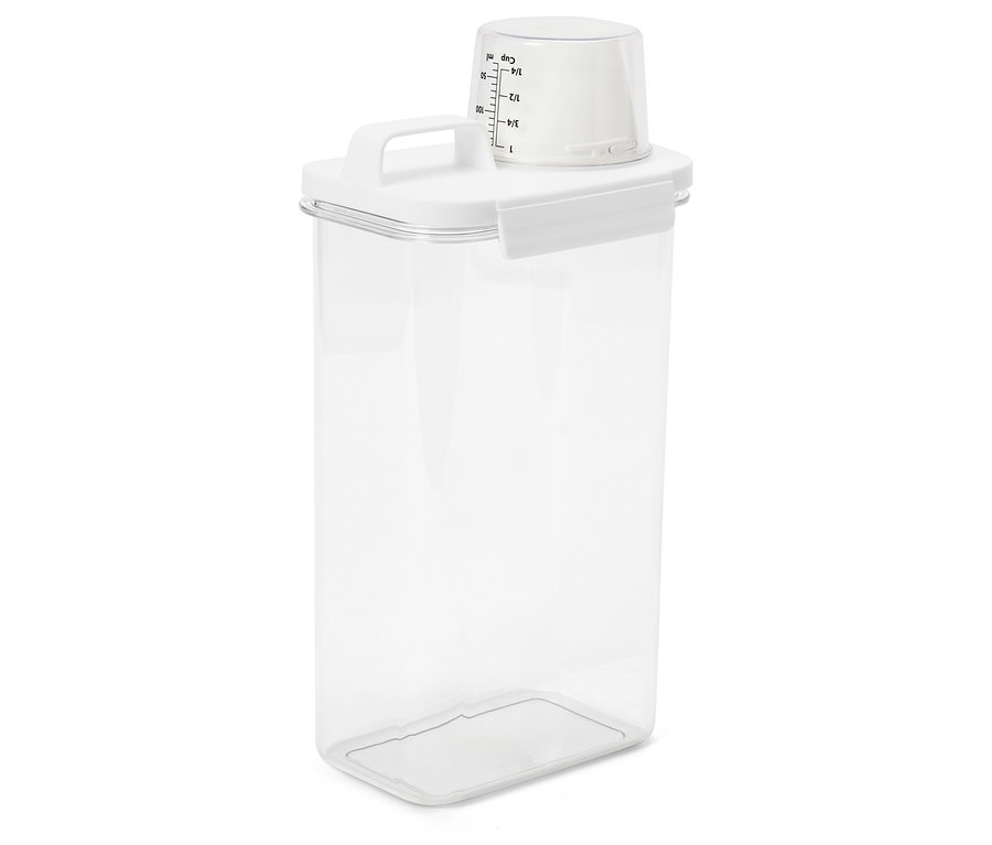 Un récipient de stockage transparent avec un couvercle blanc et une tasse à mesurer est posé sur une surface blanche.