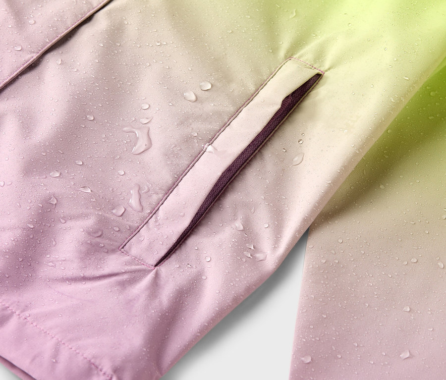 Gros plan sur une veste imperméable avec un dégradé de couleurs allant du rose au jaune avec des gouttes de pluie et une poche latérale.