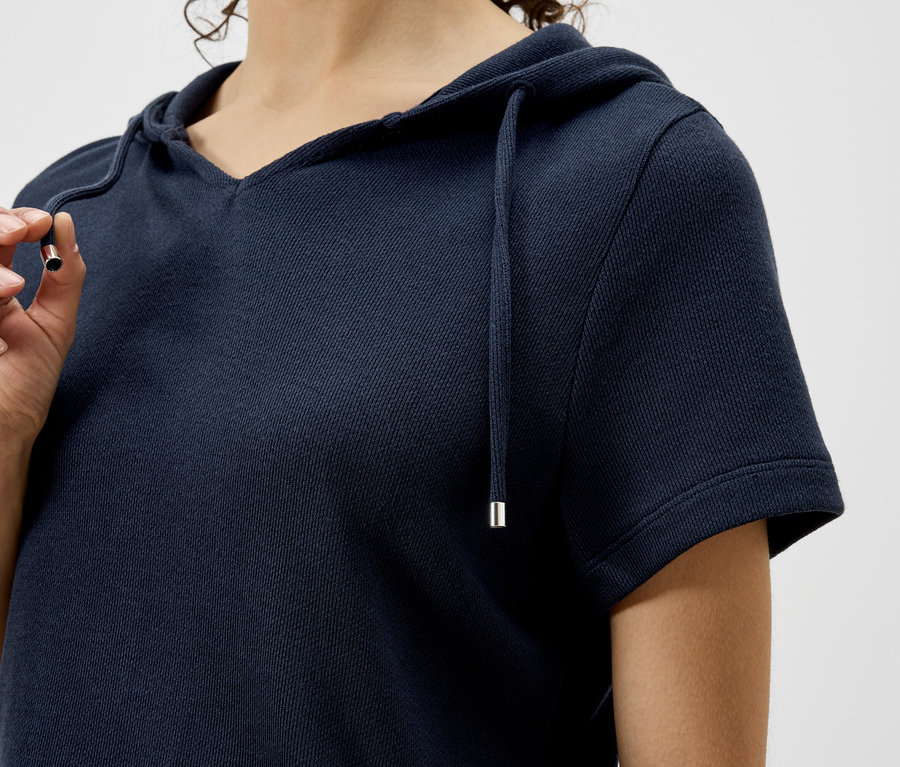 Gros plan d'une femme portant un sweat à capuche bleu marine à manches courtes et tenant un cordon.