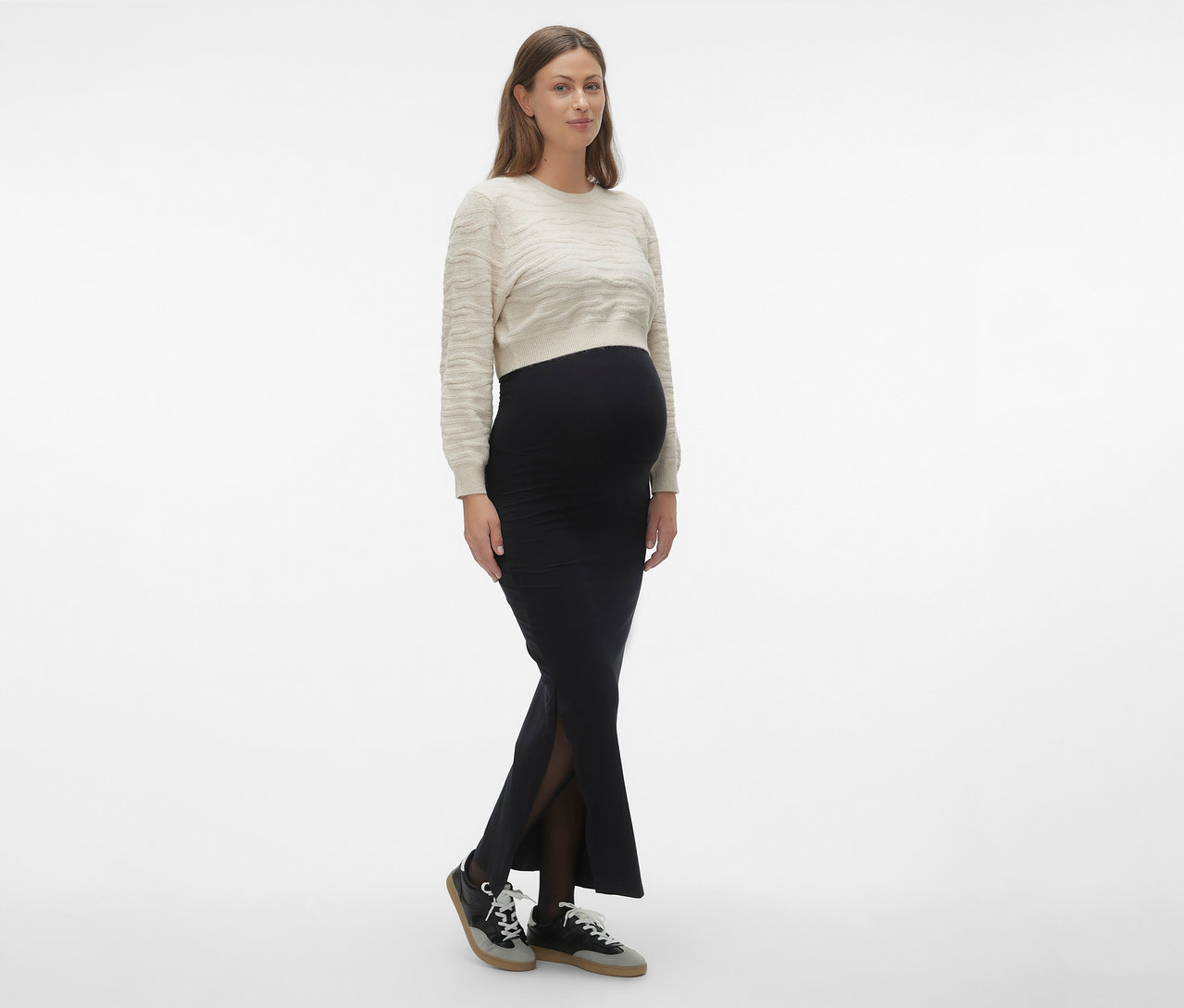 Femme portant une jupe maxi MAMALICIOUS «
MLEMMA TUBE
» noire, un pull clair et des baskets.