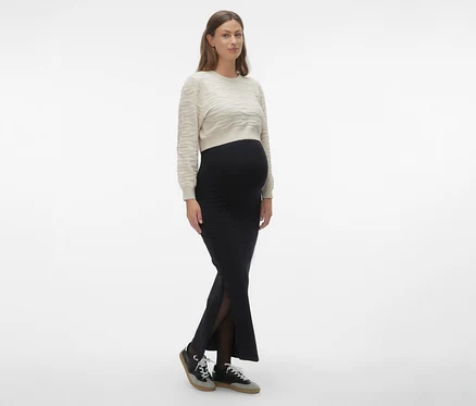 Femme portant une jupe maxi MAMALICIOUS «
MLEMMA TUBE
» noire, un pull clair et des baskets.