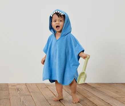 Un jeune enfant porte un poncho bleu en forme de requin et tient une pelle verte.