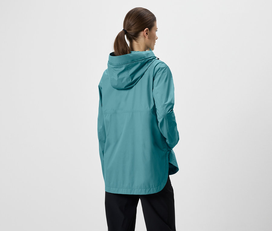 Vue arrière d'une femme avec une queue de cheval portant un imperméable turquoise à capuche et un pantalon noir sur fond blanc.