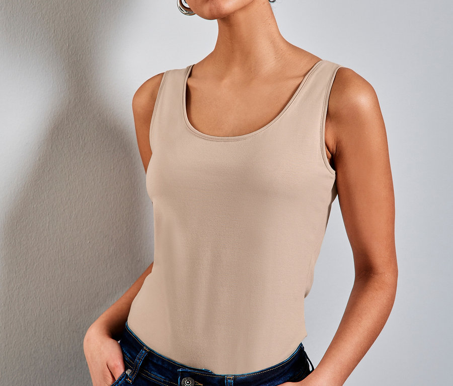 Femme aux cheveux courts et bouclés portant un haut classique Street One beige et un jean bleu foncé, les mains dans les poches.