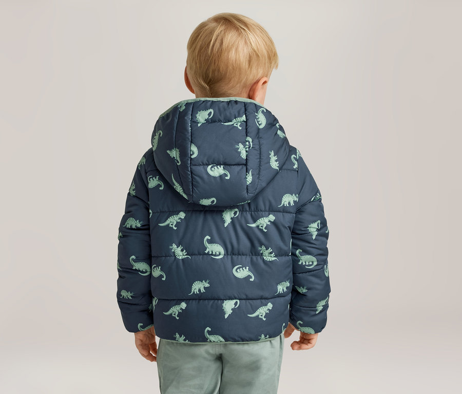 Petit garçon vu de dos, portant une veste matelassée bleu marine à capuche avec des motifs de dinosaures vert clair.